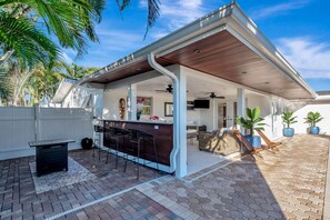 A covered outdoor patio with a bar area, seating, and potted plants.