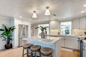 A modern kitchen with white cabinetry, a large island with stools, stainless steel appliances, and pendant lighting.