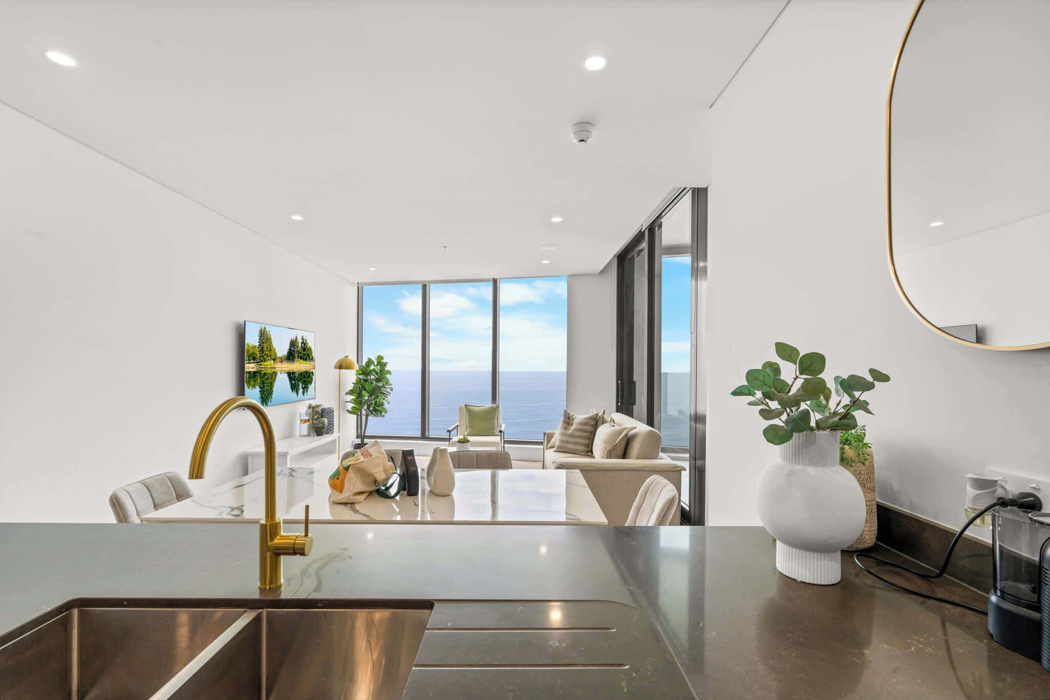 Una cocina moderna con una isla grande, un comedor con vistas y un espacio de sala con sofá y planta.