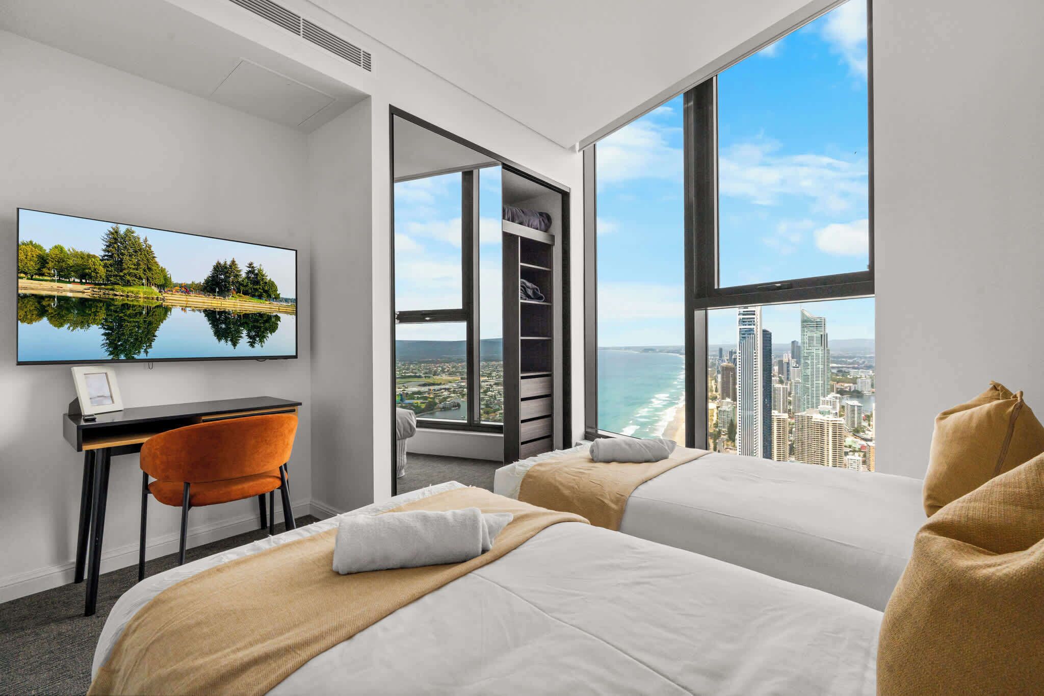 Habitación de hotel con dos camas, un escritorio, una silla, un televisor y un ventanal con vista a la ciudad.