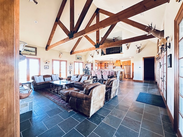A spacious living area with a high ceiling, exposed wooden beams, and a dining area with patterned chairs.