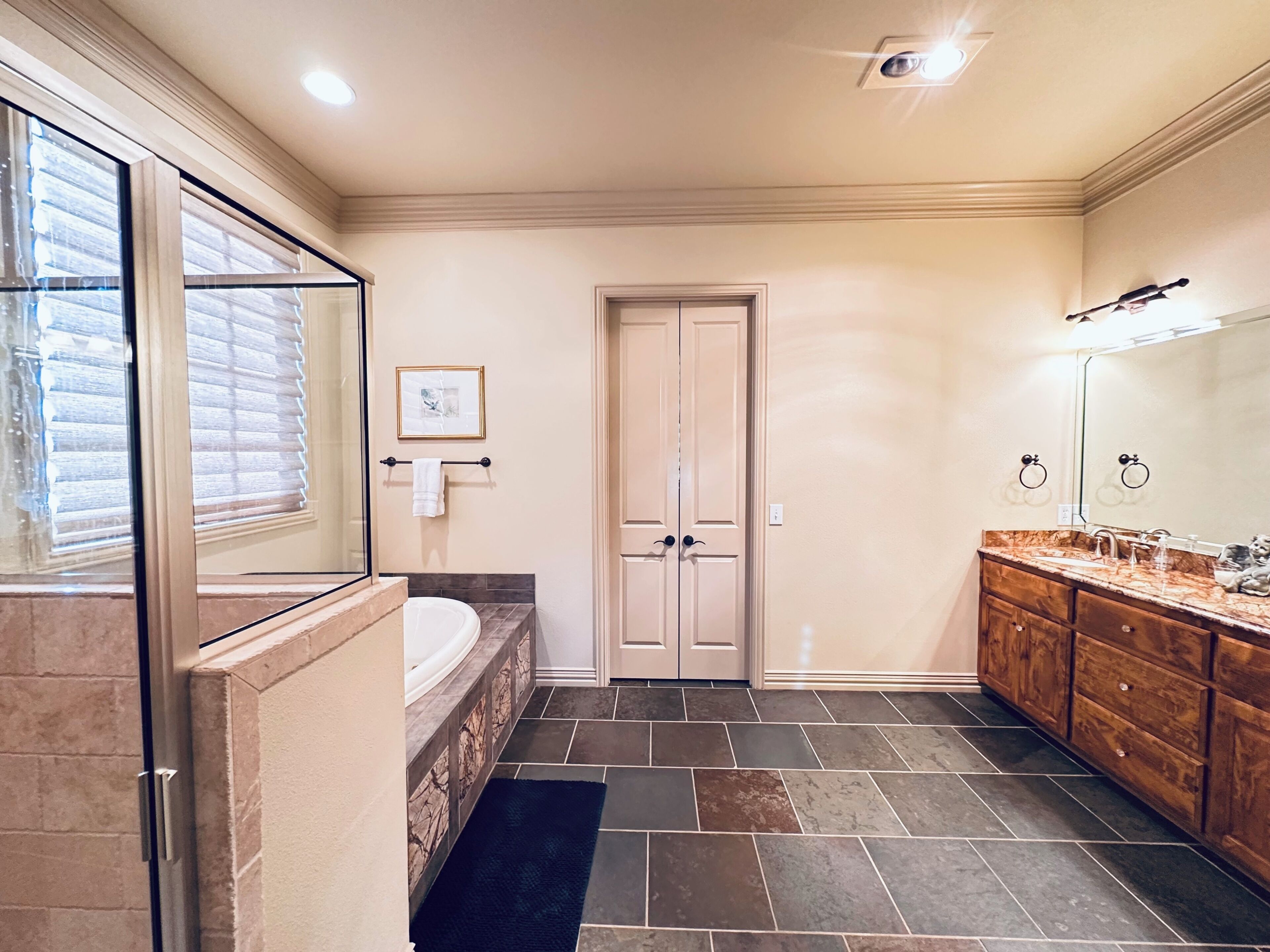 A bathroom with a bathtub, a large mirror, a vanity with a sink, and a door with a towel rack.
