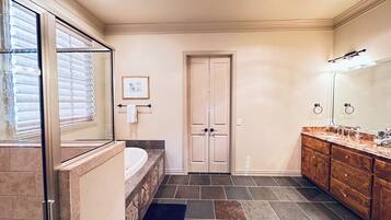 A bathroom with a bathtub, a large mirror, a vanity with a sink, and a door with a towel rack.