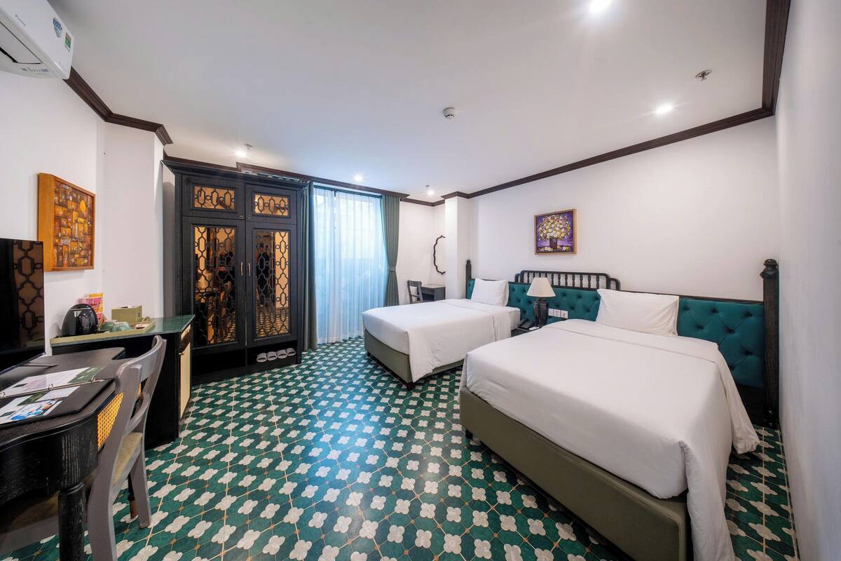 Habitación de hotel con dos camas, un escritorio con silla, televisión y piso con diseño.