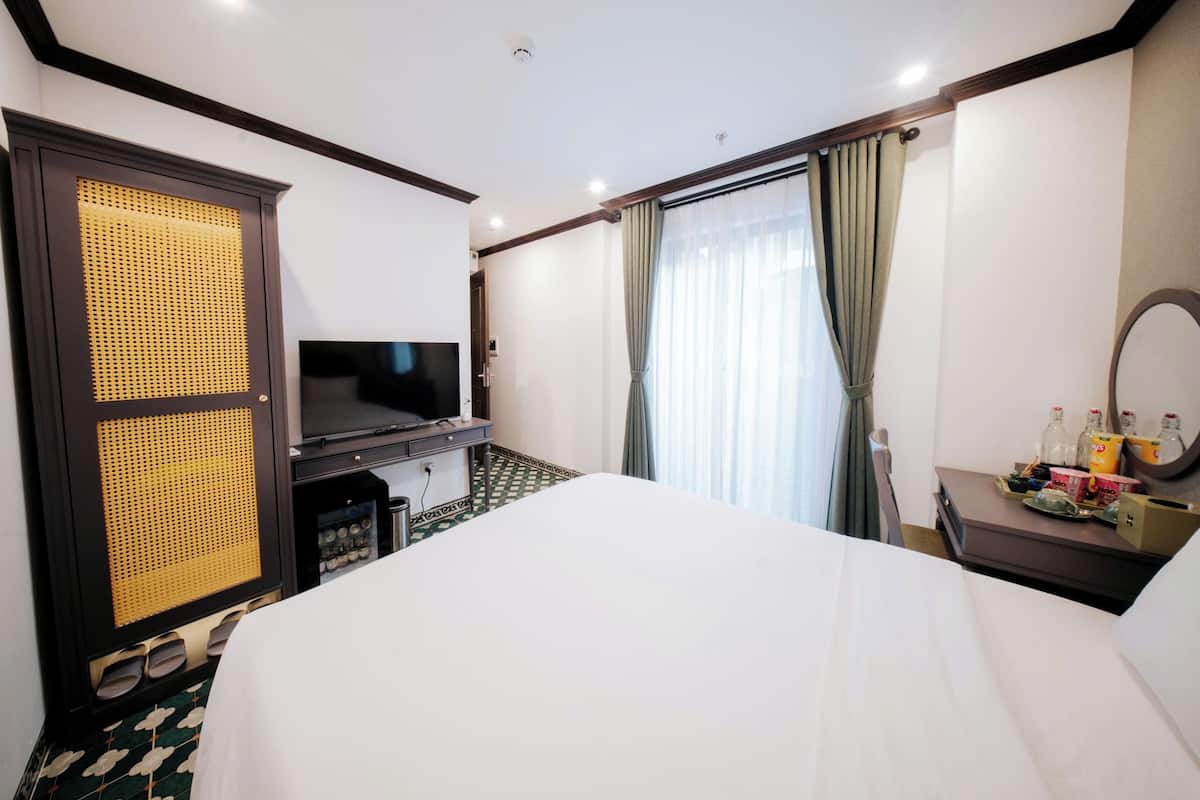 Una habitación de hotel con una cama, televisión, escritorio con espejo y ventana con cortinas.