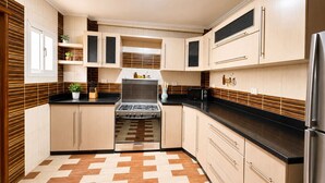 Una cocina moderna con armarios de madera clara, encimera negra, estufa a gas y refrigerador.