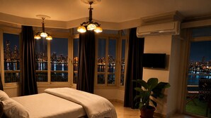 Un dormitorio con una cama, una planta en maceta, un televisor y vistas de un paisaje urbano nocturno.