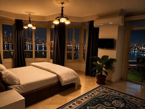 Ein Schlafzimmer mit Bett, Zimmerpflanze, Fernseher und Blick auf eine nächtliche Stadtlandschaft.