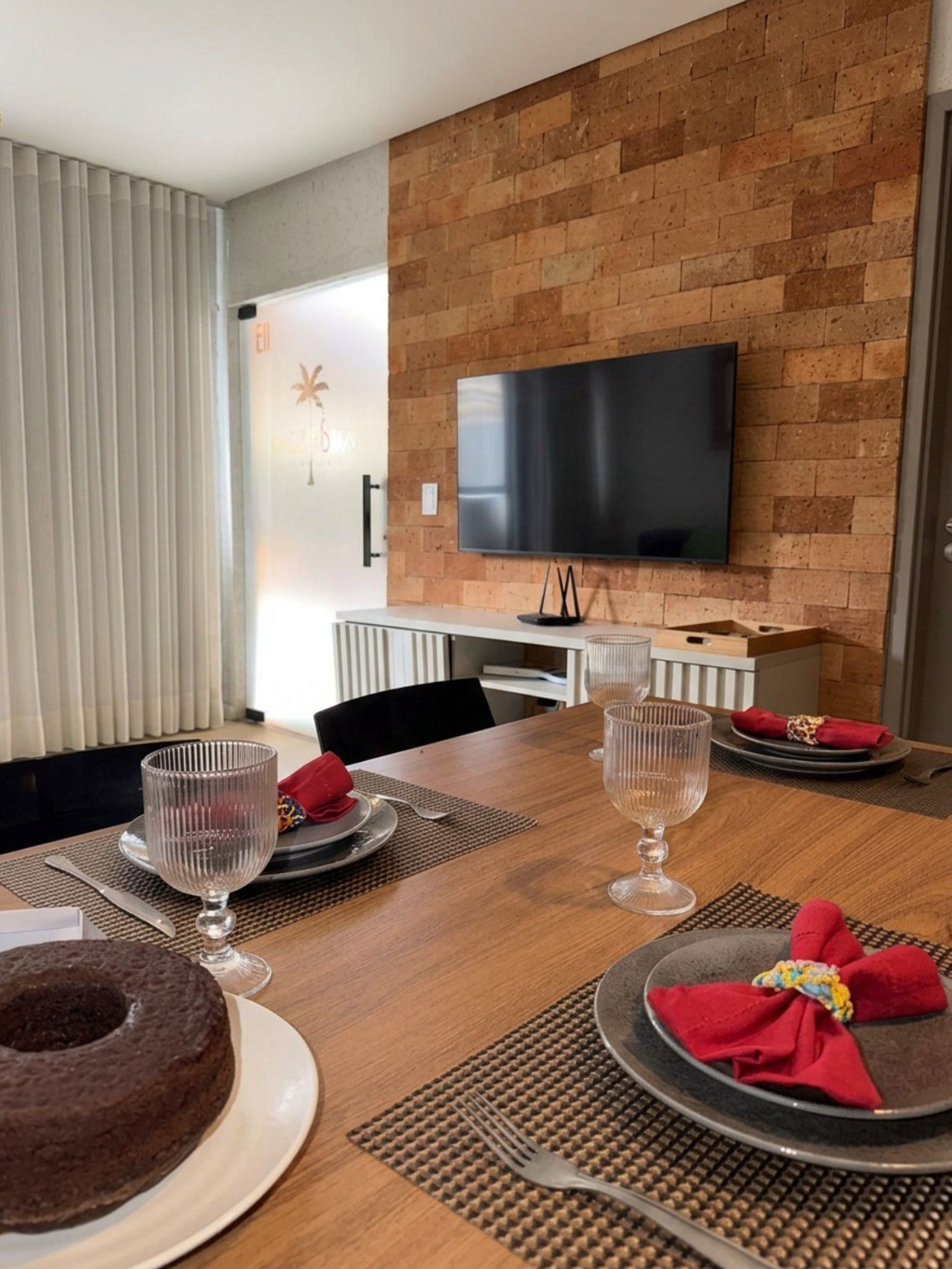 Un coin repas avec une table en bois dressée pour deux personnes, un téléviseur fixé à un mur en briques et un aménagement intérieur moderne.