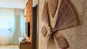 A room with a textured wall, a flat-screen TV mounted on the wall, a wooden door, and a window with sheer curtains. - MHV Milagres - Mandí 03 (São Miguel dos Milagres)