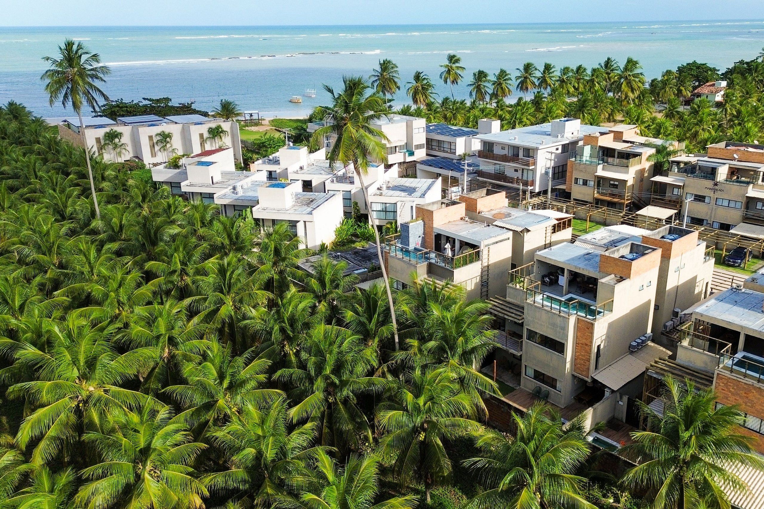 A coastal residential area with modern buildings, palm trees, and a view of the ocean.