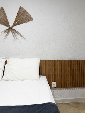 Ein Schlafzimmer mit einem Bett, weißer Bettwäsche, einem hölzernen Kopfteil und einem Wandventilator.