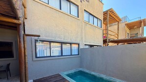 A swimming pool with a wooden deck, a window, and a building with a beige exterior. - MHV Milagres - Mandí 03 (São Miguel dos Milagres)