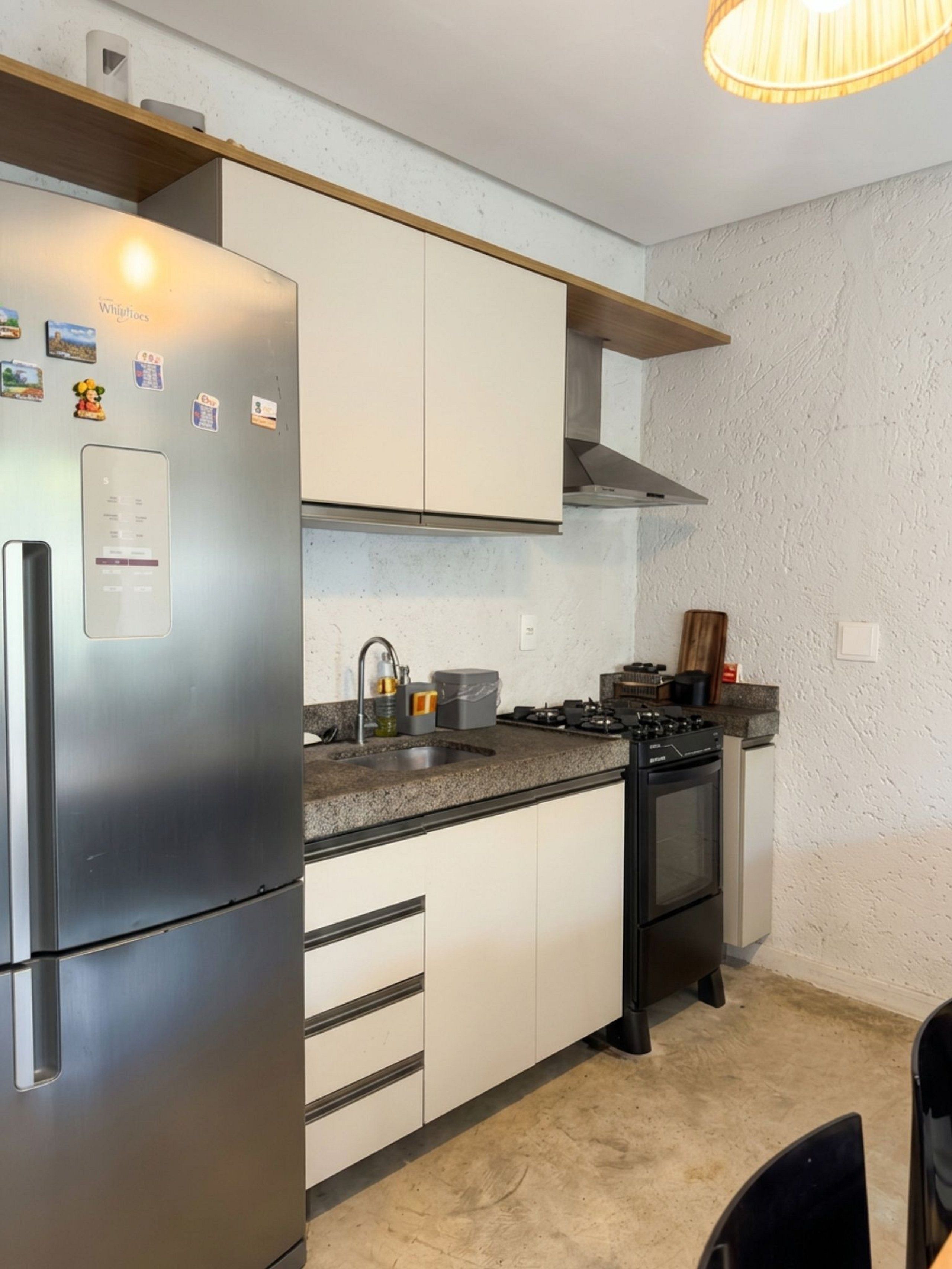 Una cocina compacta con un refrigerador de acero inoxidable, una estufa a gas y alacenas blancas.