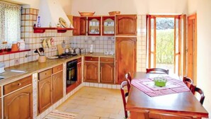 A kitchen with wooden cabinets, a dining table with chairs, and a view of greenery outside. - 6 bedroom nice home in Orbetello (Orbetello)