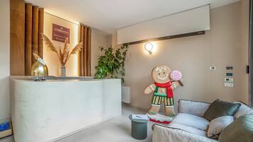 Un espace d’accueil avec un comptoir en bois, une grande décoration représentant un bonhomme en pain d’épices, une plante en pot et un canapé moderne.