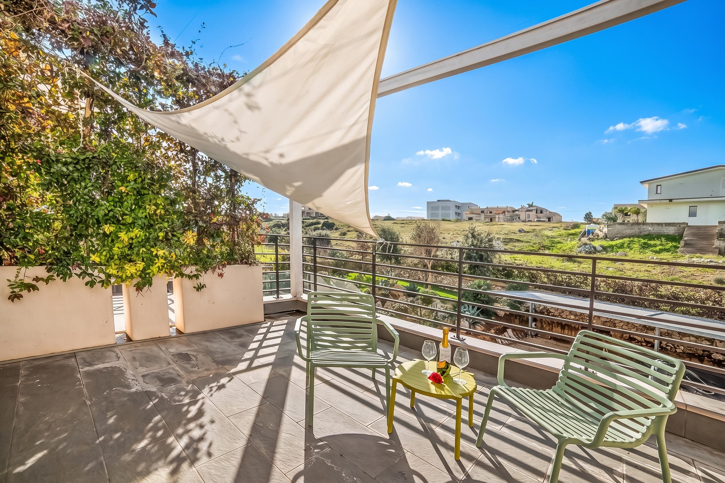 Ein Balkon mit Tisch und Stühlen, einer Champagnerflasche und Blick auf eine grüne Landschaft sowie Gebäude.