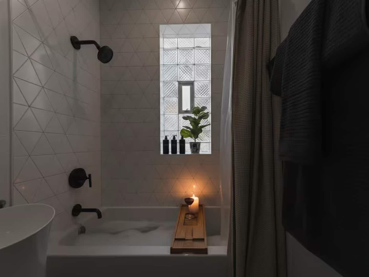 Un bagno con una vasca, una finestra con una pianta e una candela.