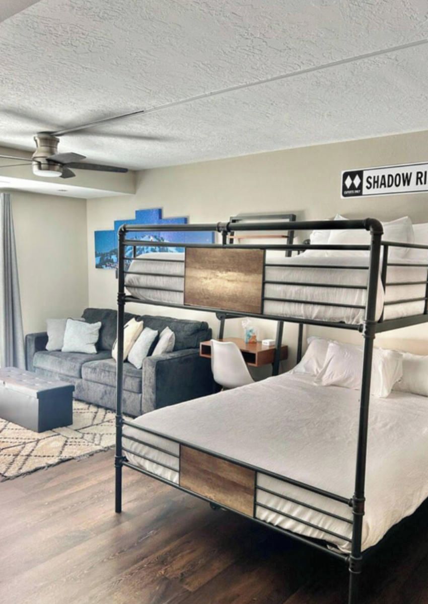 Een stapelbed met hoofdbord, een bank en een tafeltje in een kamer met een plafondventilator.