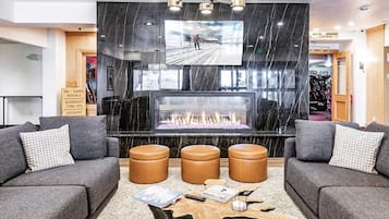 A modern lobby with a fireplace, grey sofas, and a large TV screen.
