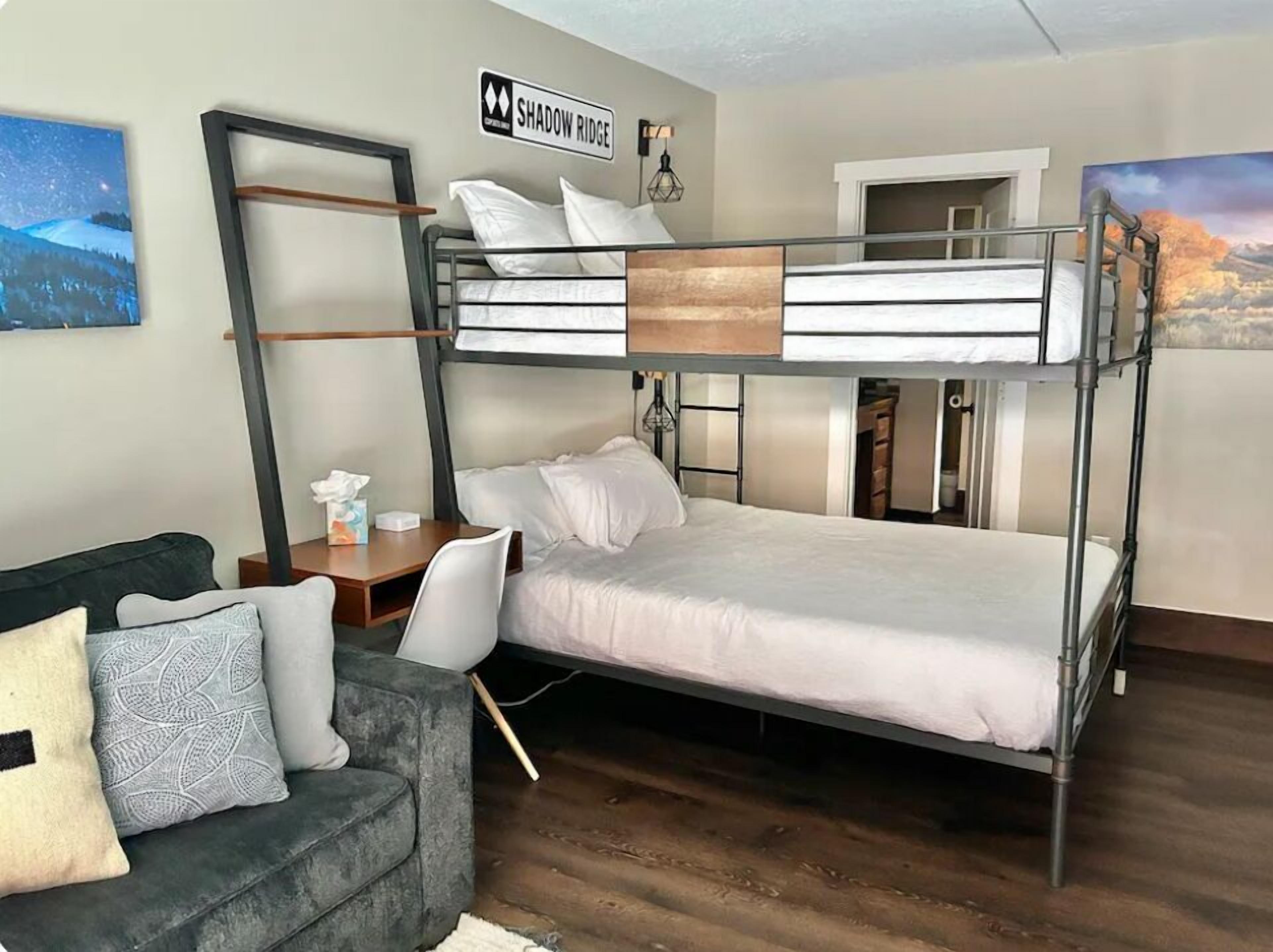 A bunk bed room with a desk, a couch, and a painting of a landscape.