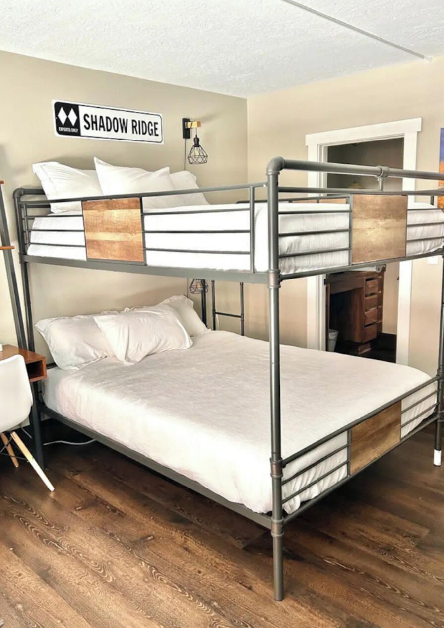 A bunk bed with a metal frame, white bedding, and a wall sign reading 'Shadow Ridge.'