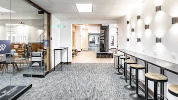 A modern office space with glass walls, a long counter with stools, and a carpeted floor.