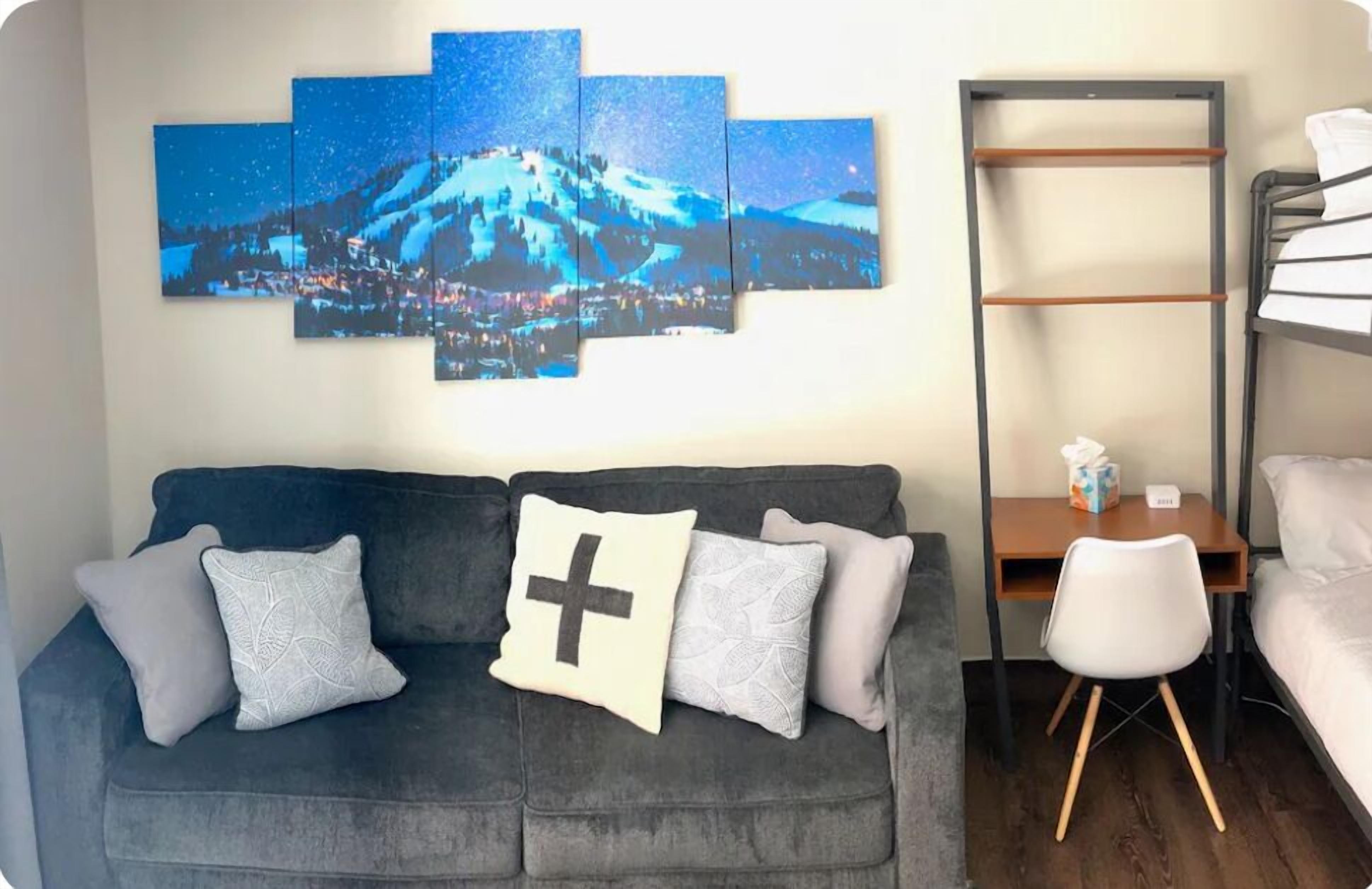 A room with a grey sofa, a small wooden desk, a white chair, and a bunk bed.