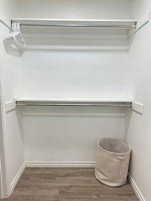 A closet with two open shelves and a trash can.