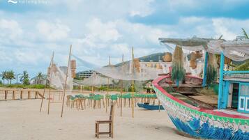 Escena de playa con un barco grande, sillas de playa y un edificio pequeño.