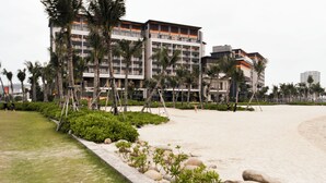 Ein Hotel mit mehreren Stockwerken, ein Strand im Hintergrund und Palmen.