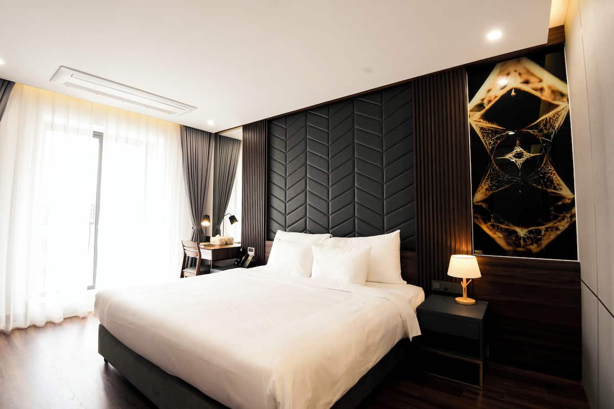Una habitación de hotel moderna con una cama grande, una mesita de noche, una lámpara y un panel decorativo en la pared.