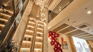 Eine moderne Hotelhalle mit einem Marmor-Rezeptionsschalter, einer vertikalen Leuchte und einer Wand mit roten floralen Verzierungen.
