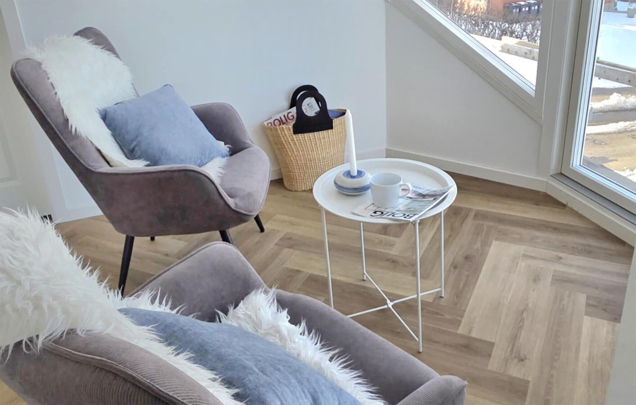 Ein modernes Wohnzimmer mit einem grauen Sessel, einem kleinen runden Tisch mit einer Zeitschrift und einem Korbwannen-Korb.