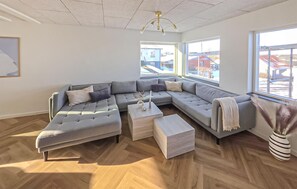 A spacious living room with a large L-shaped sectional sofa, a wooden coffee table, and a view of the outside through large windows. - 4 bedroom beautiful home in Farsø (Farsø)