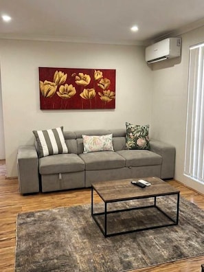 A living room with a grey sofa, a coffee table, and a red floral painting.