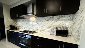 A modern kitchen with dark cabinets, a stainless steel range hood, a built-in oven, and a marble backsplash. - 31 Kids, Coast & Chill - 4BR Parking & Theatre Rm (Secret Harbour)