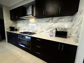 A modern kitchen with dark cabinets, a stainless steel range hood, a built-in oven, and a marble backsplash. - 31 Kids, Coast & Chill - 4BR Parking & Theatre Rm (Secret Harbour)
