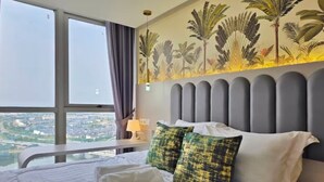 Een hotelkamer met een groot bed, uitzicht op de stad door het raam en een muurschildering met tropische motieven.