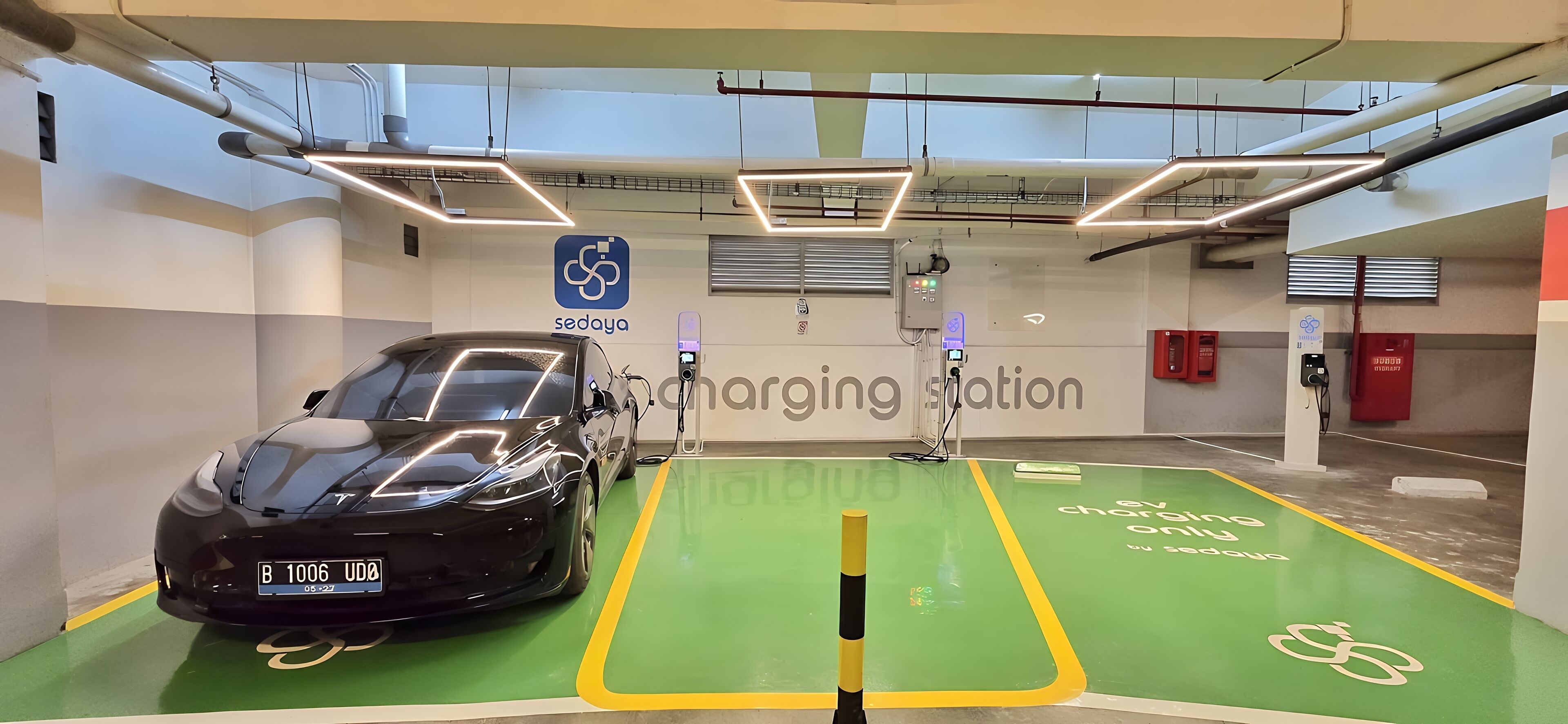 Une borne de recharge pour voitures avec un sol vert, une voiture noire et un panneau indiquant « Sedoya ».