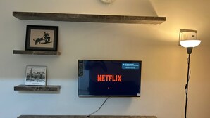Een flatscreen televisie aan de muur, waarop het Netflix-logo te zien is, met een marmeren kast eronder en een ingelijste foto erboven.