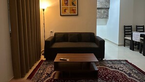 Een woonkamer met een bank, een salontafel, een gekleurd tapijt, een lamp en een lijstwerk aan de muur.