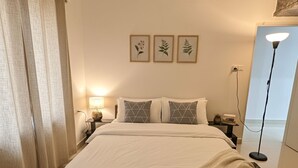 Een net opgemaakt bed met witte lakens, een bedlampje en een lijst met een botanische afbeelding aan de muur.