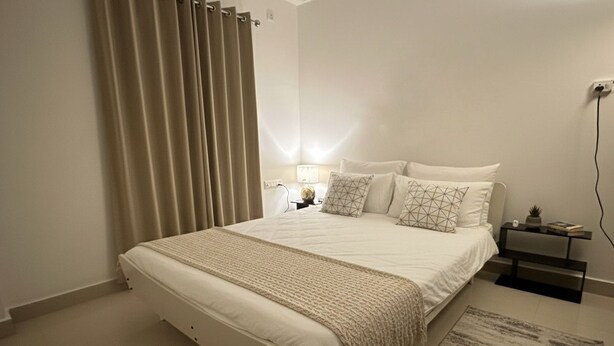 Een slaapkamer met een bed, nachtkastje, lamp en nachttafeltje.