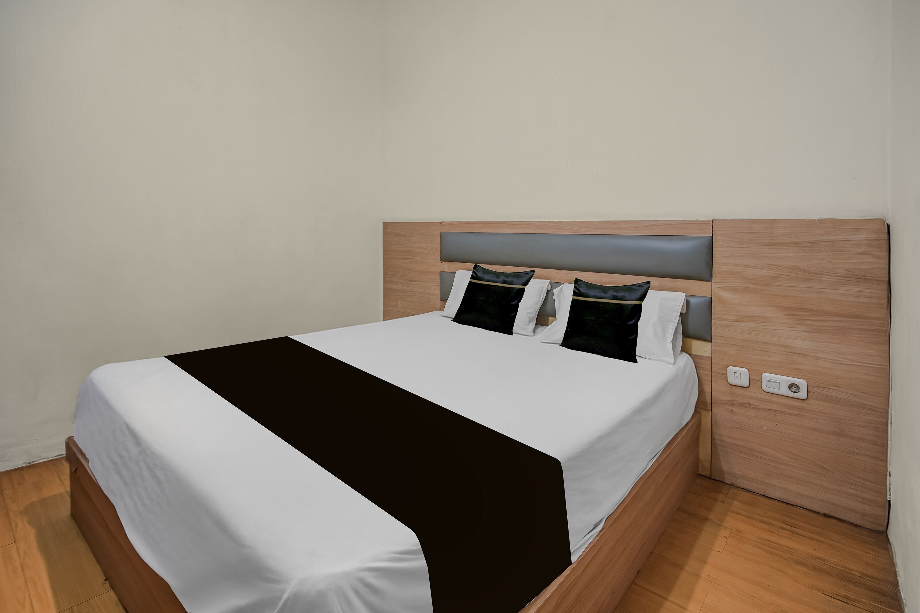 A neatly made bed with a white and black bedspread, a wooden headboard, and a nightstand with a power outlet.
