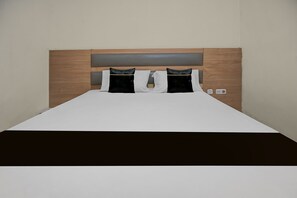Habitación de hotel con cabecera de madera, colcha blanca y dos almohadas negras.