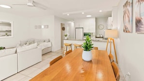 Un salón moderno con una mesa de comedor de madera, sofá blanco y una cocina al fondo.