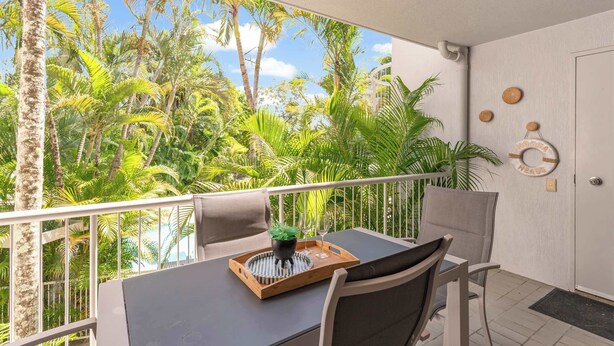 Un balcón con vistas a follaje tropical, una mesa con bandeja y una silla.