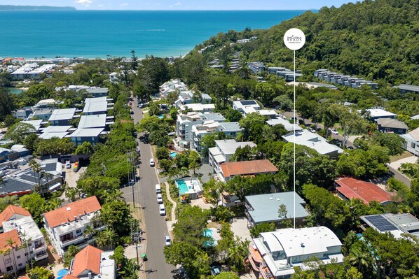 An aerial view of a residential area with multiple buildings, a swimming pool, and a view of the ocean.