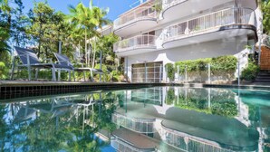 A multi-story hotel with balconies, a swimming pool, and surrounding greenery. - Noosa Hill Getaway - Walk to Beach + Shared Pool (Noosa Region)